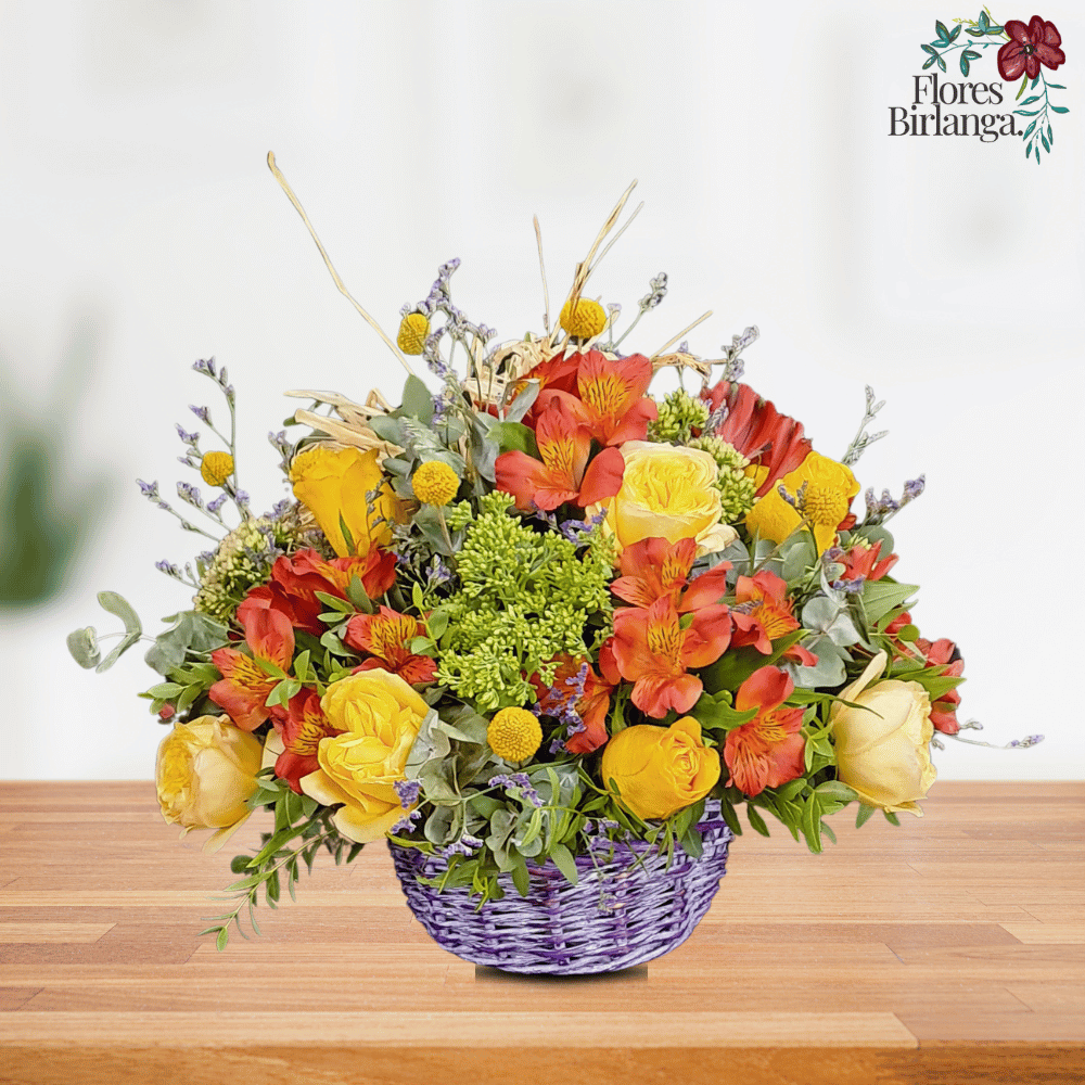 Cesta de mimbre color lavanda con flores naturales: romelia, rosas amarillas, sedum, craspedia, eucalipto y limonium, sobre mesa de madera.