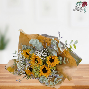 Ramo de 6 girasoles con gypsophila, eucalipto y verdes decorativos, envuelto en papel kraft y negro sobre mesa de madera.