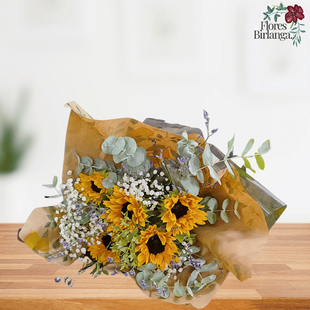 Ramo de 6 girasoles con gypsophila, eucalipto y verdes decorativos, envuelto en papel kraft y negro sobre mesa de madera.